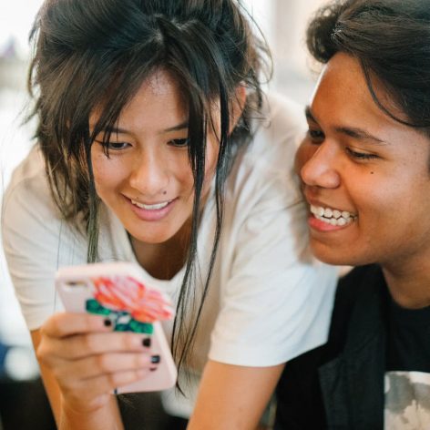 two teens smile looking at a phone