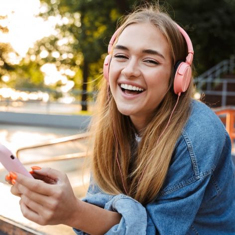 smiling teenage girl wearing headphones and holding phone